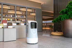 A modern hotel lobby with a reception desk, a self-service kiosk, and a large potted plant. - Ji Hotel (Hangzhou)