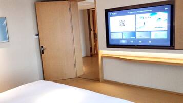 A hotel room with a bed, a TV mounted on the wall, and a door leading to another room.