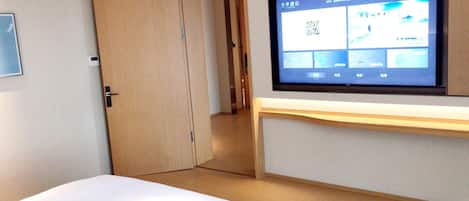 Een hotelkamer met een bed, een aan de muur bevestigde televisie en een deur naar een andere kamer.