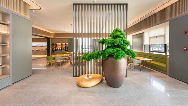 Un hall d’entrée moderne agrémenté d’une grande plante en pot, d’une sculpture en bois et d’un espace détente avec des tables et des chaises.