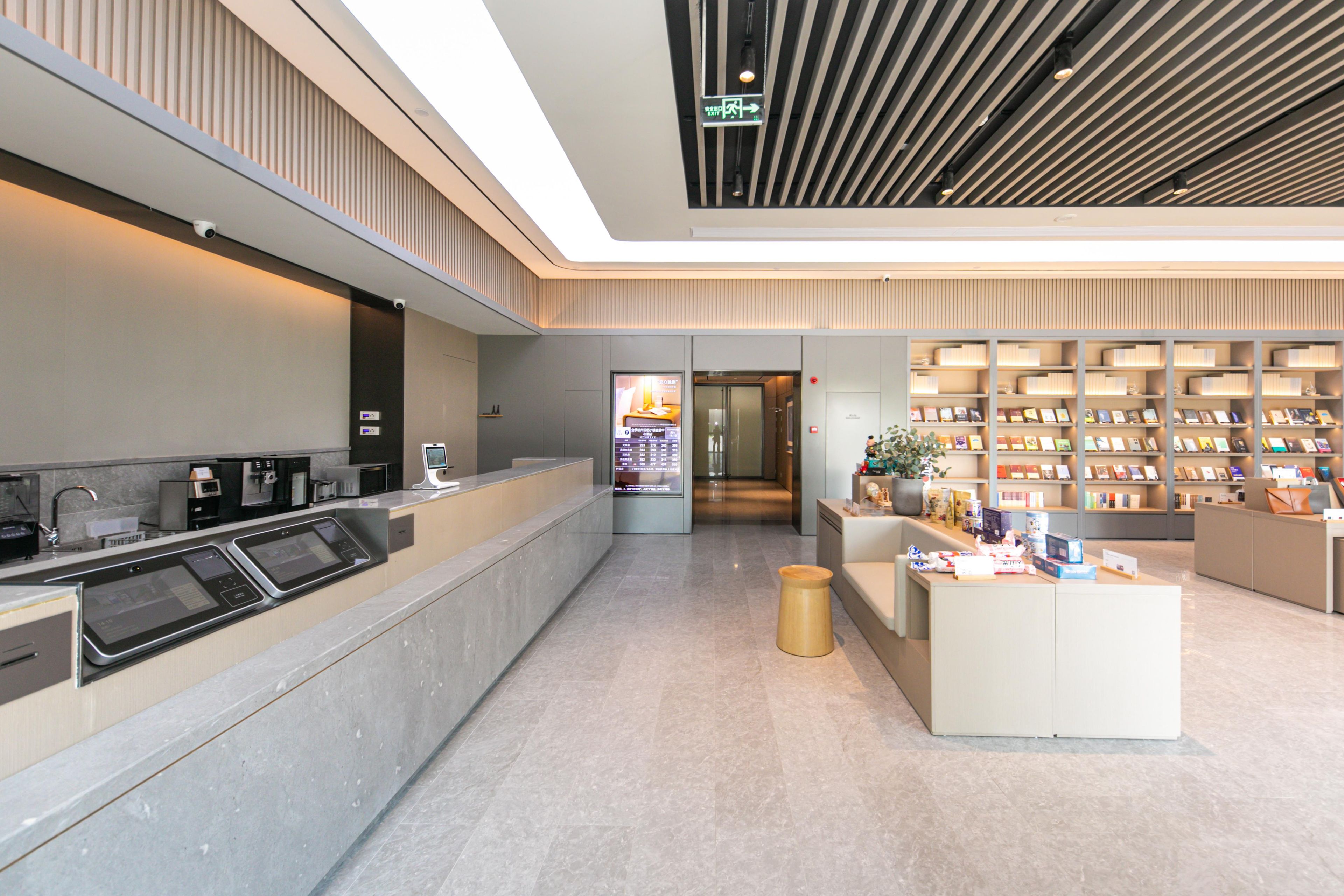 A modern reception area with a digital check-in kiosk, a waiting area with seating, and a bookstore with bookshelves.