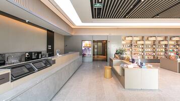A modern reception area with a digital check-in kiosk, a waiting area with seating, and a bookstore with bookshelves.