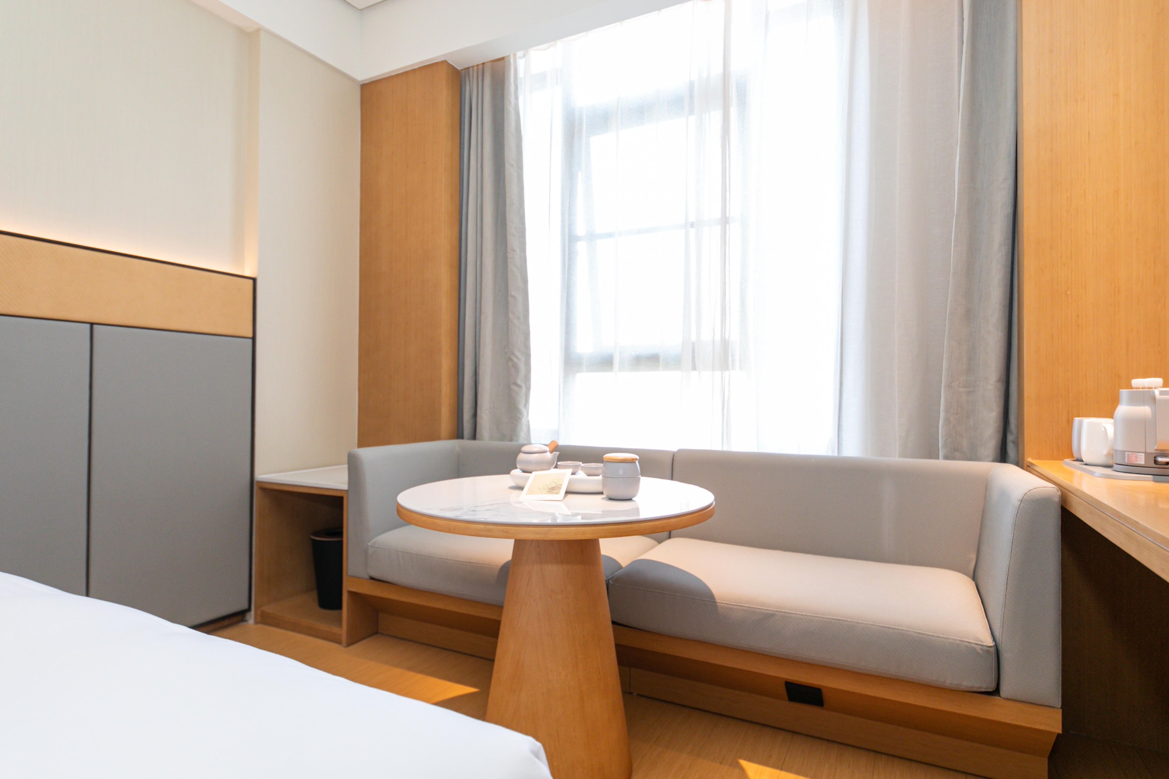 Una habitación de hotel moderna con sofá, una mesa redonda y una ventana con cortinas.