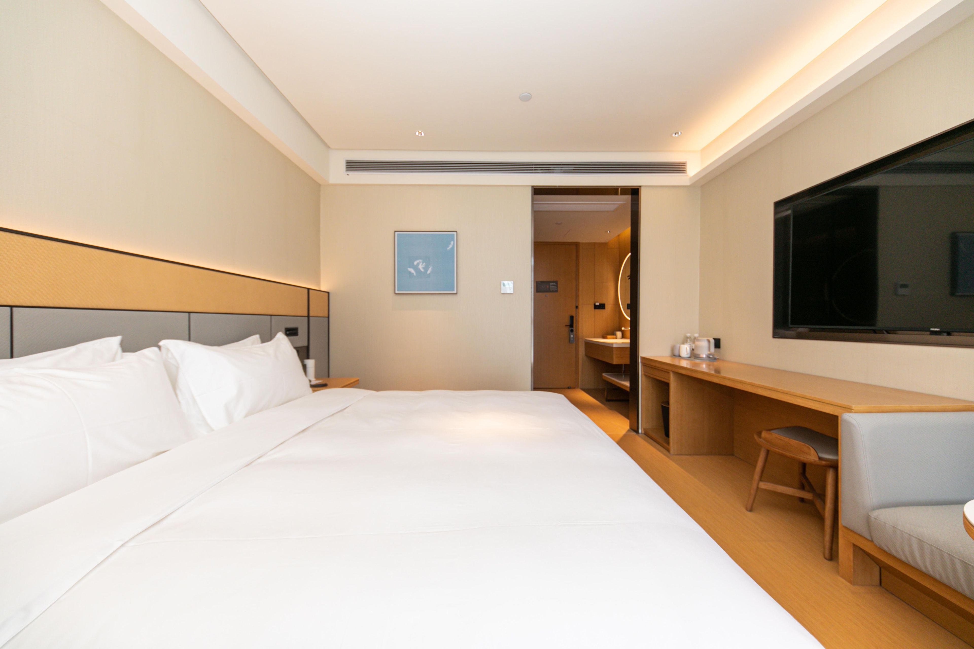 Une chambre d’hôtel avec un grand lit, un bureau, une chaise, une télévision et une salle de bain visible à travers une porte ouverte.