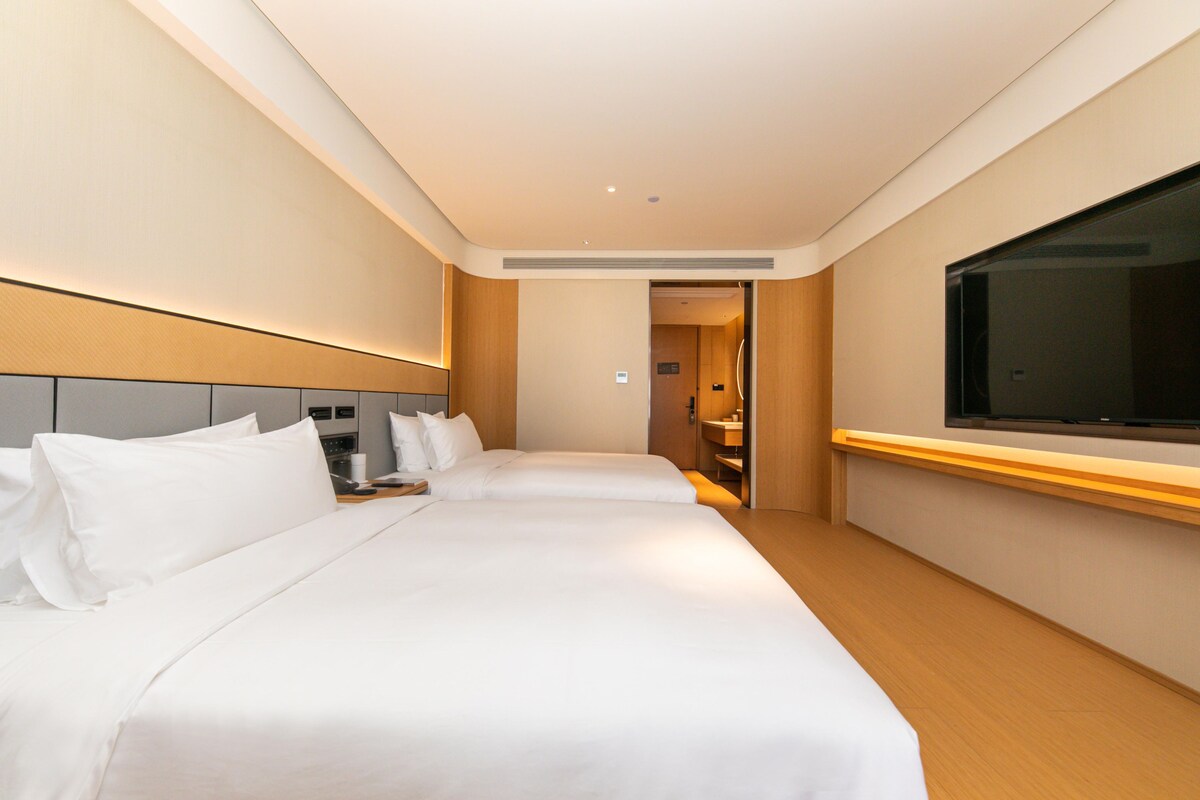 A hotel room with two beds, a TV, and a bathroom visible through an open door.