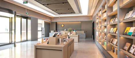 A modern reception area with a reception desk, a digital display, and a bookshelf with books.