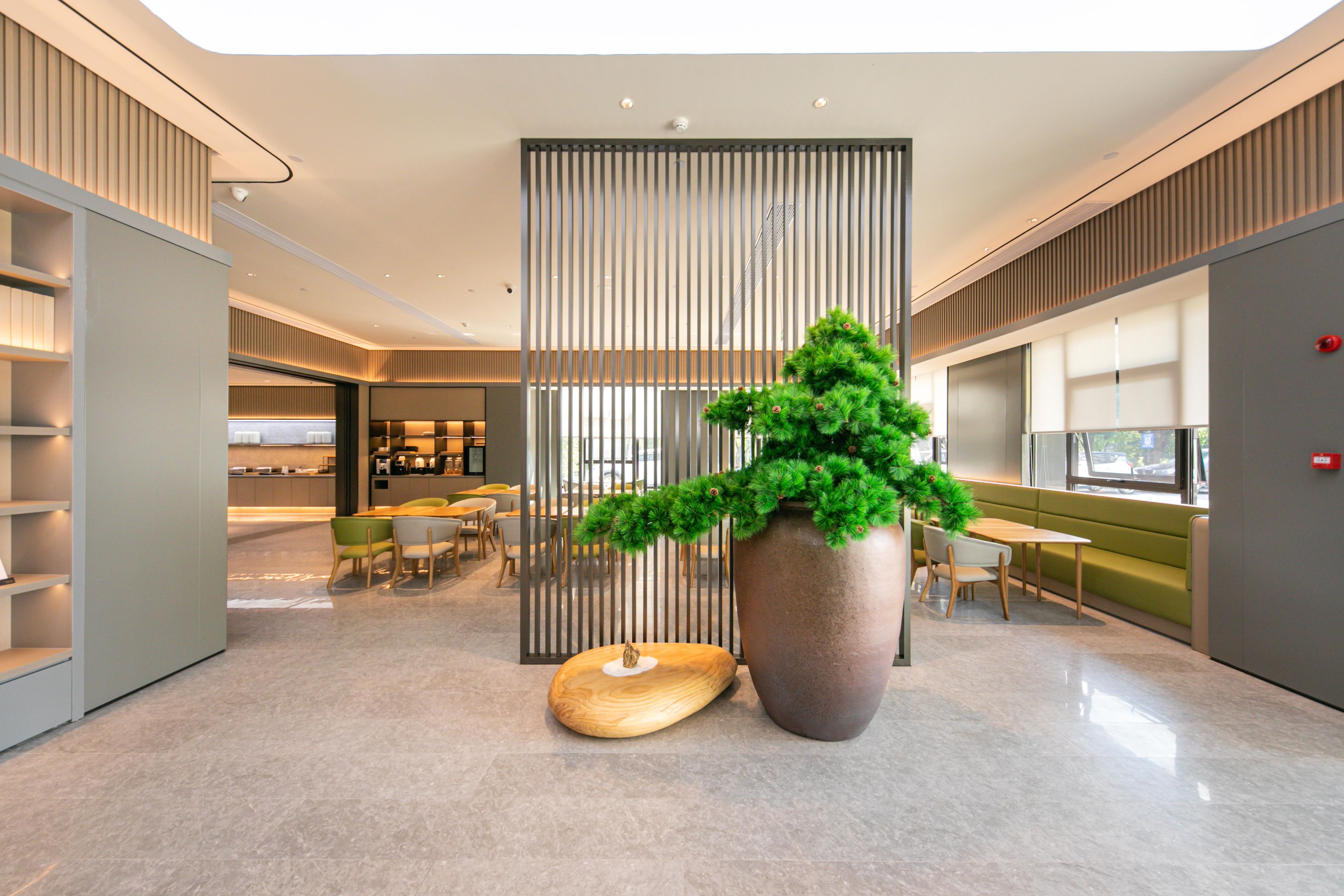 A modern lobby with a large potted plant, a wooden sculpture, and a seating area with tables and chairs.