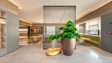 A modern lobby with a large potted plant, a wooden sculpture, and a seating area with tables and chairs.