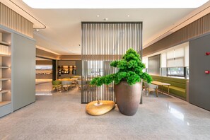 A modern lobby with a large potted plant, a wooden sculpture, and a seating area with tables and chairs. - Ji Hotel (Hangzhou)