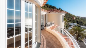 A curved balcony with a white railing, large windows, and a view of a hillside. - Sunnyside Villa with private pool - 10 min from the beach! (Calheta)