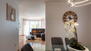 A modern living room with a sofa, coffee table, and chairs. There is a large clock on the wall and a vase with flowers on the table. - Sunnyside Villa with private pool - 10 min from the beach! (Calheta)