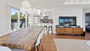 Una cocina moderna con una mesa de comedor de madera, sillas blancas e iluminación colgante.