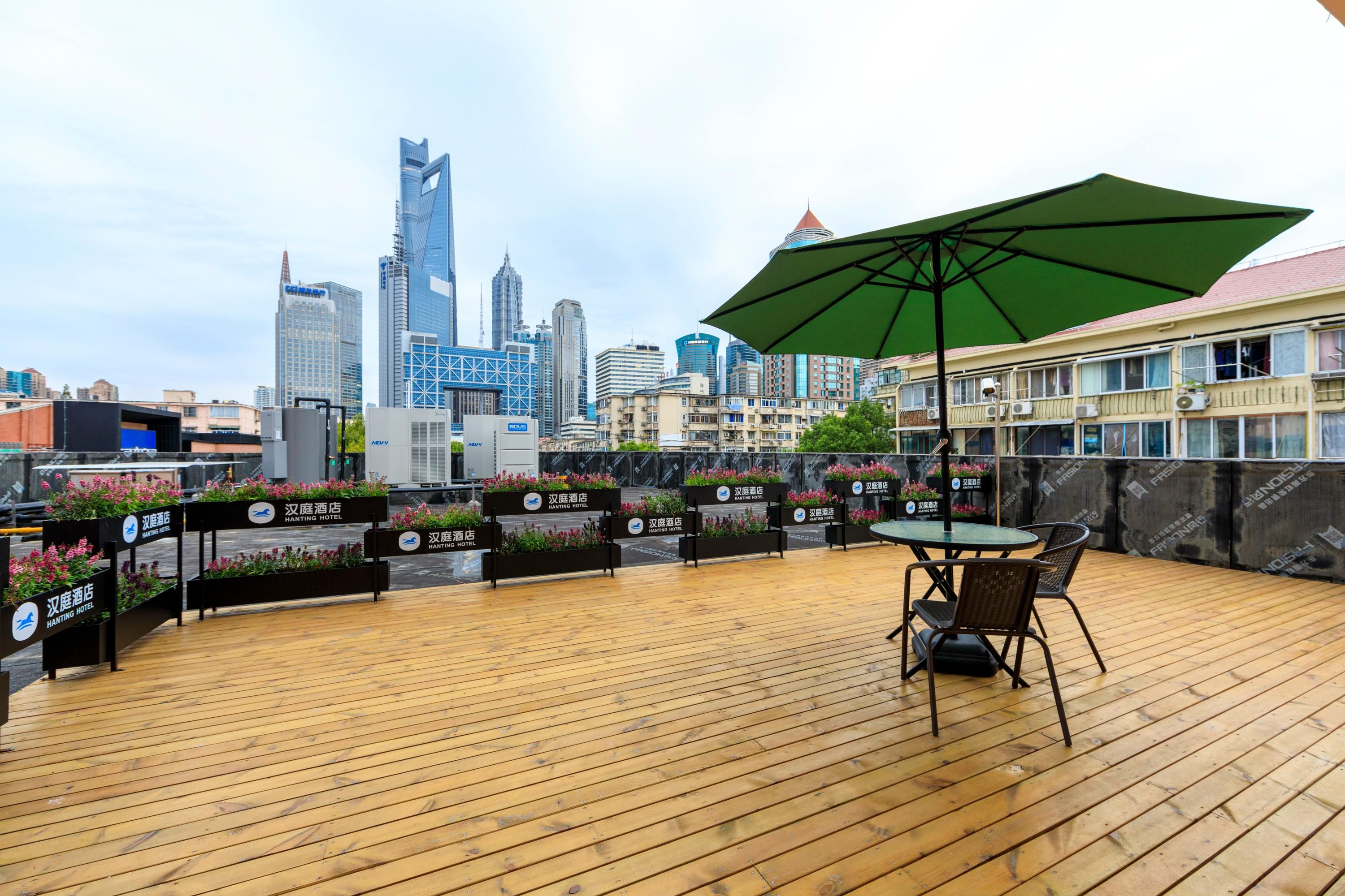 A rooftop terrace with wooden flooring, a table with chairs, a green umbrella, and signage for 'Hanwick Hotel.'