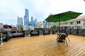 Une terrasse sur le toit avec un plancher en bois, une table avec des chaises, un parasol vert et une enseigne indiquant « Hôtel Hanwick ».