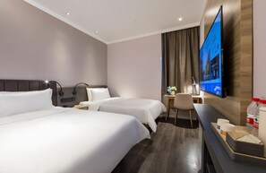 Habitación de hotel con dos camas, un escritorio, un televisor y una pequeña mesa con un jarrón de flores.