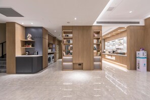 Un moderno vestíbulo de hotel con mostrador de recepción, máquina de café, lavadora e interior bien iluminado.
