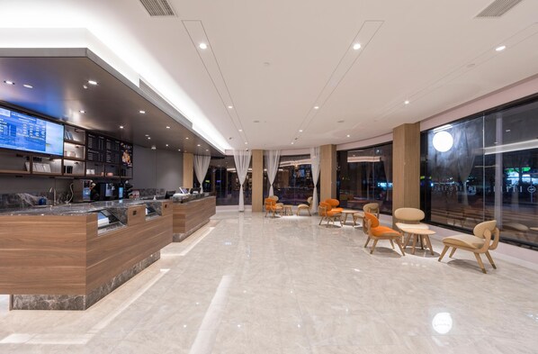 Un hall d’hôtel moderne avec un comptoir d’accueil, un espace salon et de grandes fenêtres.