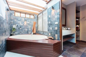 Un baño moderno con una bañera independiente, paredes de baldosas de piedra, un tragaluz y un espejo grande.