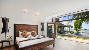 A modern bedroom with a large bed, a view of a swimming pool, and a glass door leading to an outdoor area. - TED Villas (Koh Samui)