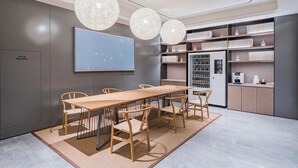 A modern meeting room with a long table, chairs, a large screen, and a refrigerator. - JI Hotel (Shanghai)