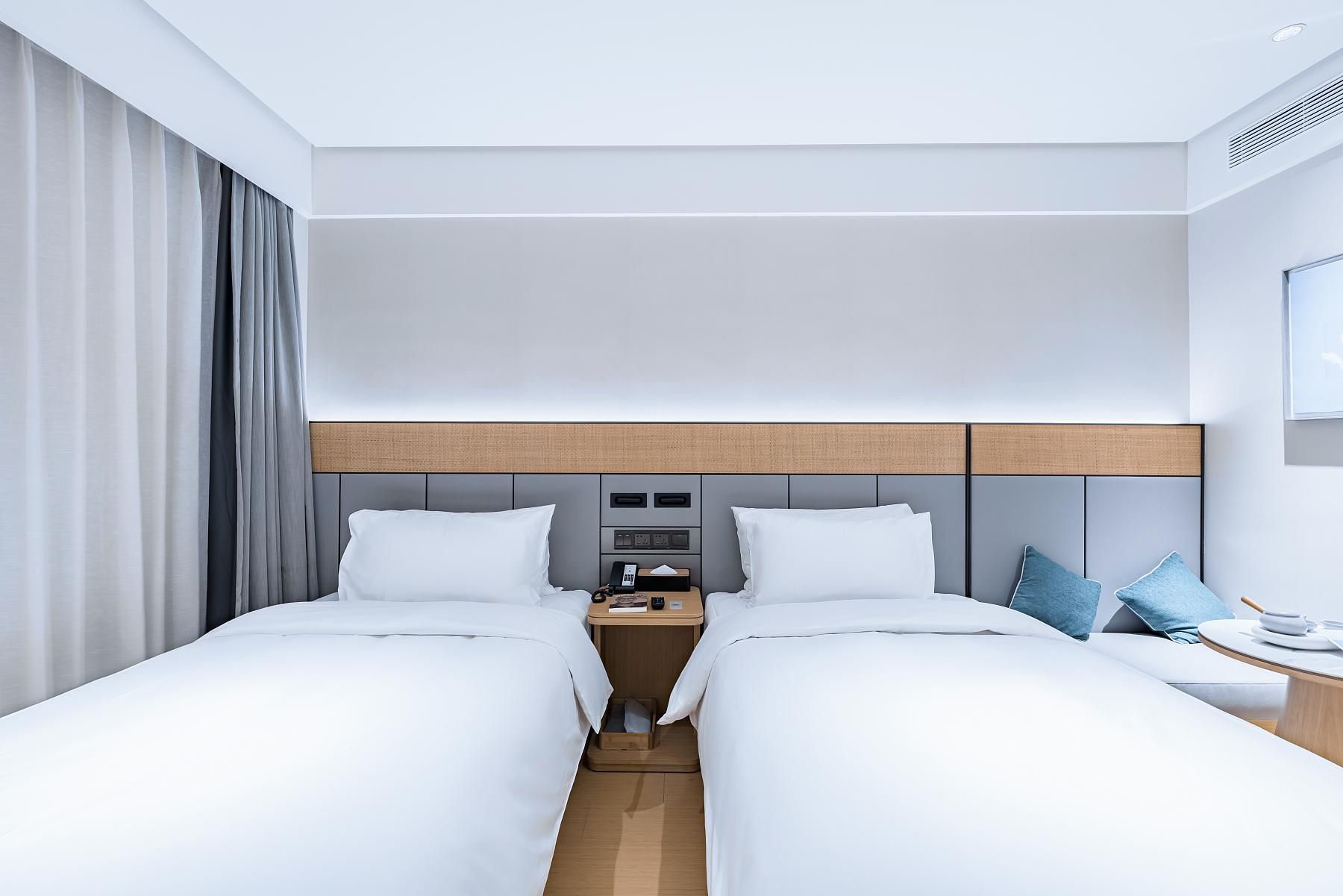 Ein modernes Hotelzimmer mit einem großen Bett, einem Nachttisch, einem Fernseher und einem Fenster mit Vorhängen.