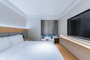 Une chambre d’hôtel moderne avec un grand lit, un coin salon avec une table et une grande fenêtre.
