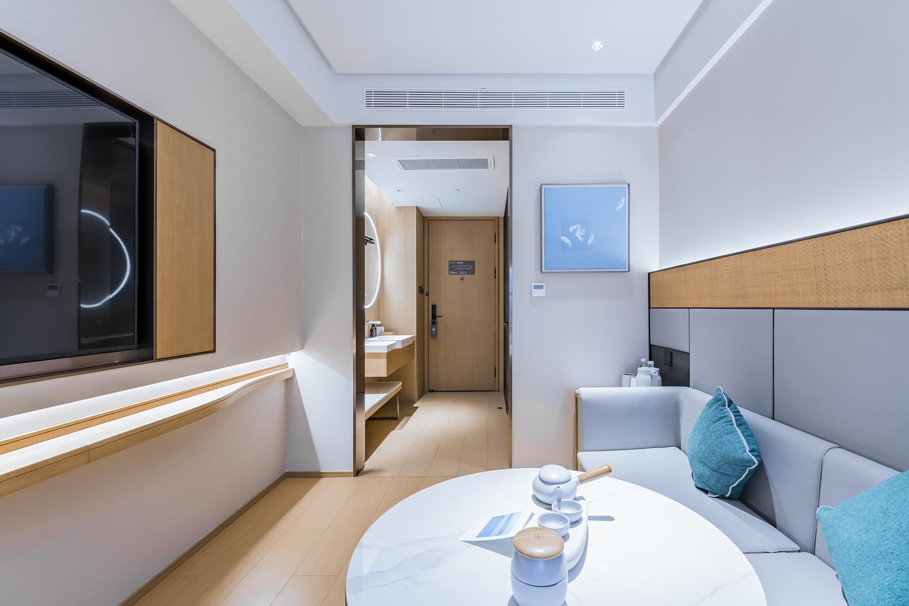 Una habitación de hotel moderna con una cama, una mesita de noche con juego de té, un ventanal y vistas al pasillo.