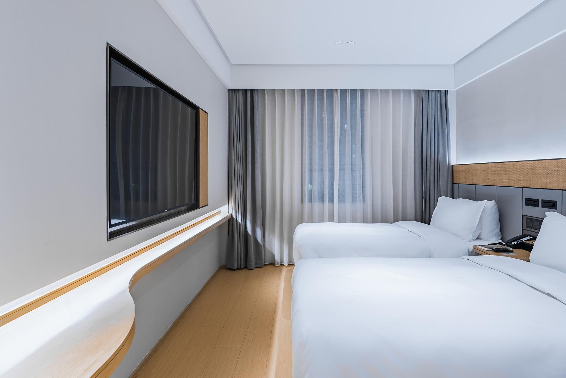 A hotel room with two beds, a large window, a curtain, and a wooden headboard.