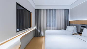 A hotel room with two beds, a large window, a curtain, and a wooden headboard.