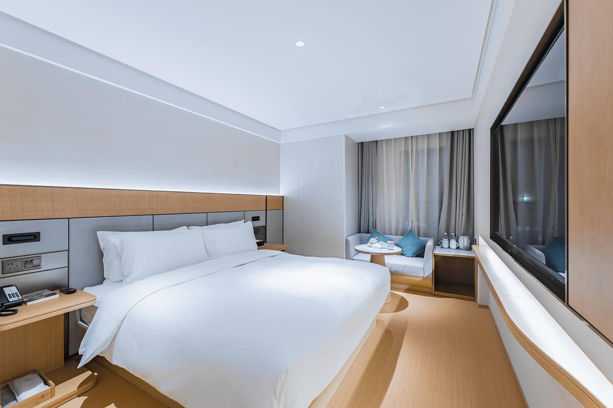 Une chambre d’hôtel avec un lit, une table de chevet, une lampe et une fenêtre avec des rideaux.