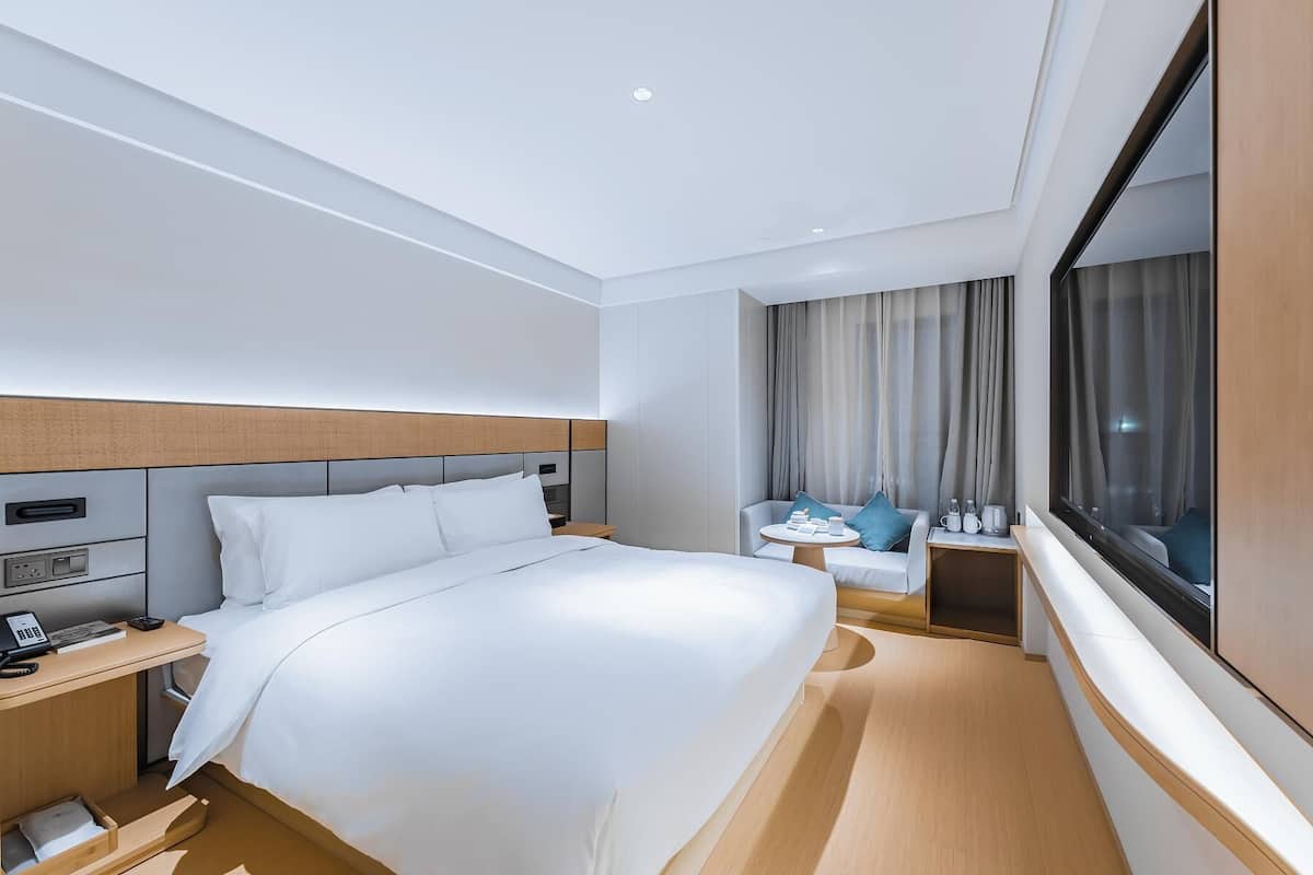 Une chambre d’hôtel avec un lit, une table de chevet, une lampe et une fenêtre avec des rideaux.