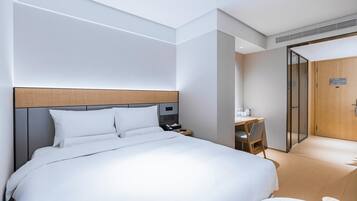 A modern hotel room with a large bed, bedside table, and a small desk with a chair.
