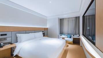 Ein Hotelzimmer mit Bett, Nachttisch, Lampe und einem Fenster mit Vorhängen.