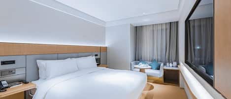 A hotel room with a bed, bedside table, lamp, and a window with curtains.