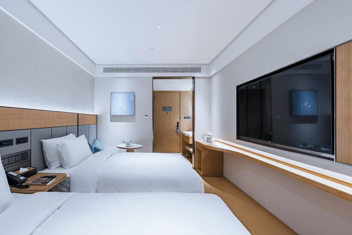 Une chambre d’hôtel avec deux lits, une télévision, une table de chevet, une petite table ronde et une porte donnant accès à la salle de bain.
