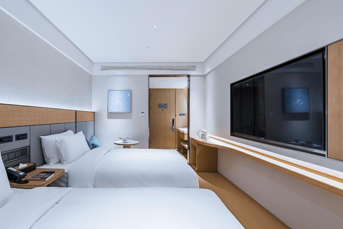 Une chambre d’hôtel avec deux lits, une télévision, une table de chevet, une petite table ronde et une porte donnant accès à la salle de bain.