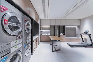 Une chambre d’hôtel moderne équipée d’un coin buanderie, d’une petite kitchenette, d’une table et d’un tapis de course.