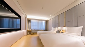 Habitación de hotel con una cama grande, mesitas de noche, televisión y ventana con cortinas.
