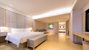 Habitación de hotel moderna con una cama grande, un banco, un escritorio y un baño visible a través de una puerta abierta.
