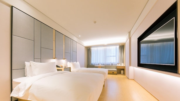 Una habitación de hotel con dos camas, un ventanal grande y un televisor de pantalla plana.