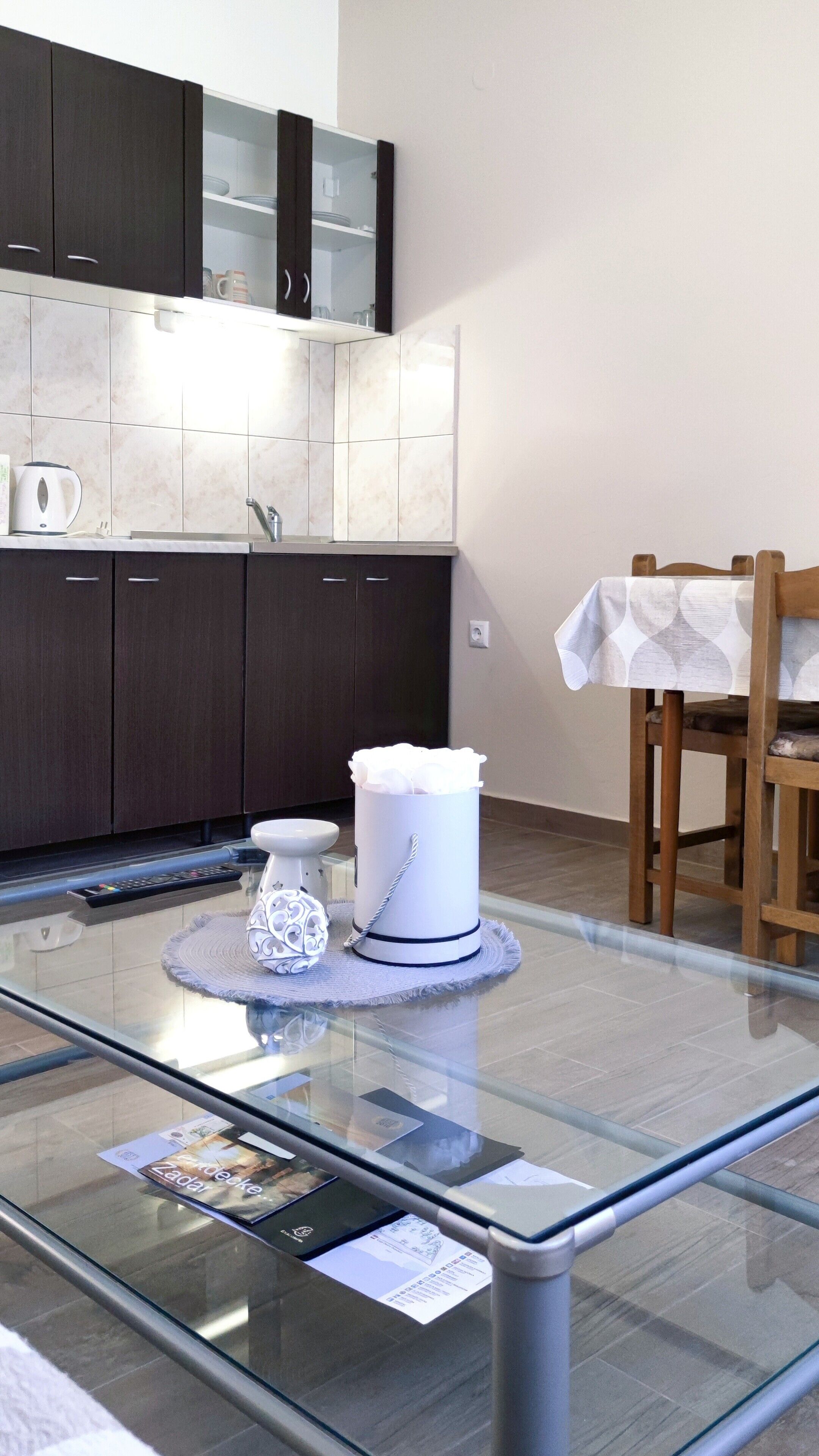 A modern kitchen with dark cabinets, a glass-top dining table, and a white vase on the table.