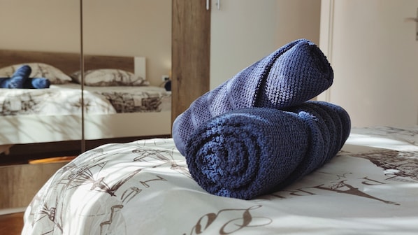 A neatly made bed with a patterned bedspread and a rolled blue towel on it.