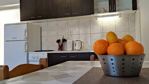 Keittiössä on jääkaappi, liesi ja pöytä, jonka päällä on kulho täynnä appelsiineja.