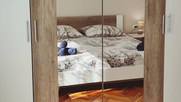 Een slaapkamer met een spiegelkast, een bed met beddengoed met patroon, en een houten visgraatvloer.