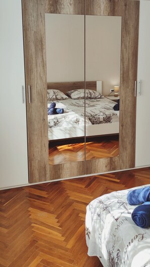 Una camera da letto con un armadio a specchio, un letto con copriletto decorato e un pavimento in legno a spina di pesce.