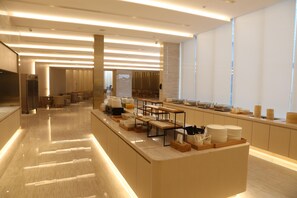 A modern kitchen area with a long counter, various kitchen appliances, and a seating area with tables and chairs. - Ji Hotel (Nanjing)