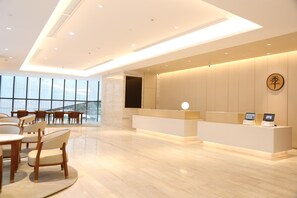 A modern hotel lobby with a reception desk, seating area, and large windows. - Ji Hotel (Nanjing)