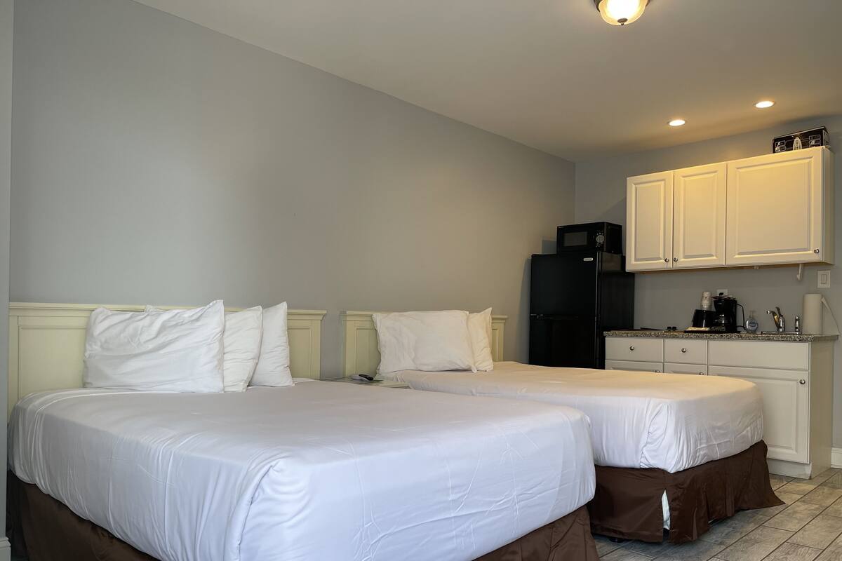 A hotel room with two beds, a kitchenette, and a small bathroom.