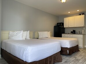 Een hotelkamer met twee bedden, een kitchenette en een kleine badkamer.