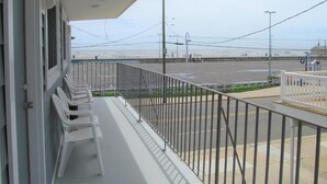 A balcony with white plastic chairs, a railing, and a view of a beach and parking lot. - Rio Motel and Suites (Wildwood)